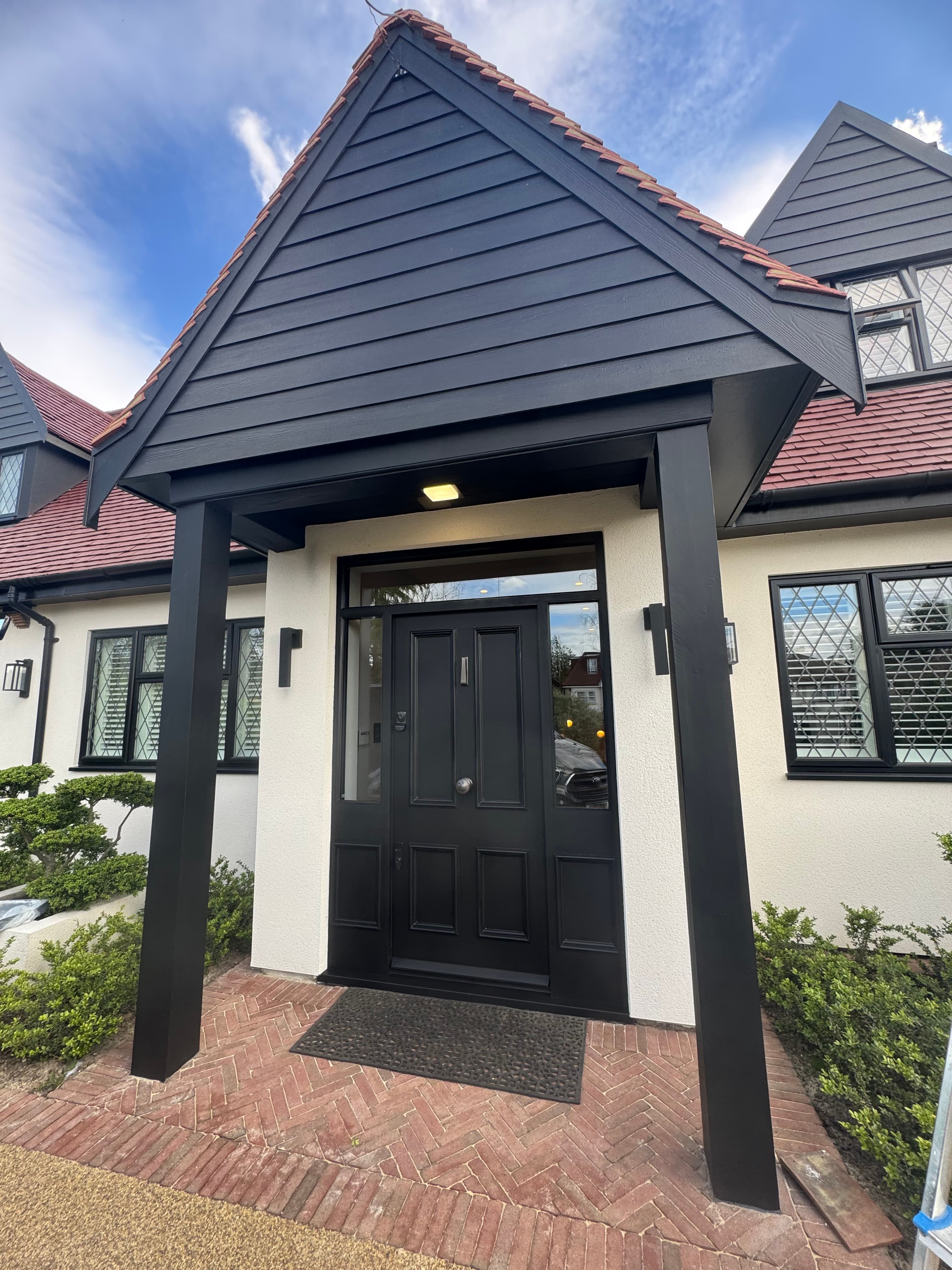 Black front door under a gabled porch with white walls and herringbone brick walkway.